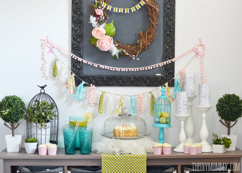 A Fresh & Happy Dessert Table Idea for Spring! A DIY wreath and DIY fabric scrap tassle banner take center stage in this fun aqua, blush pink, moss green and yellow dessert table featuring bird cages, birch candles, feathers and greenery.