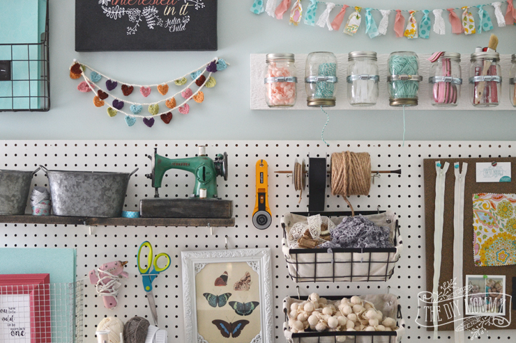 A beautiful, colorful craft room office wall with pegboard for storage, baskets, #DIY garlands, art and hanging mason jar storage.