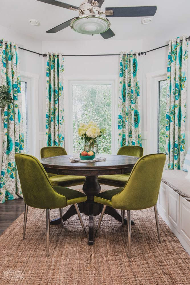 Colorful kitchen breakfast nook featuring a farmhouse table, turquoise drapes and velvet midcentury modern chairs