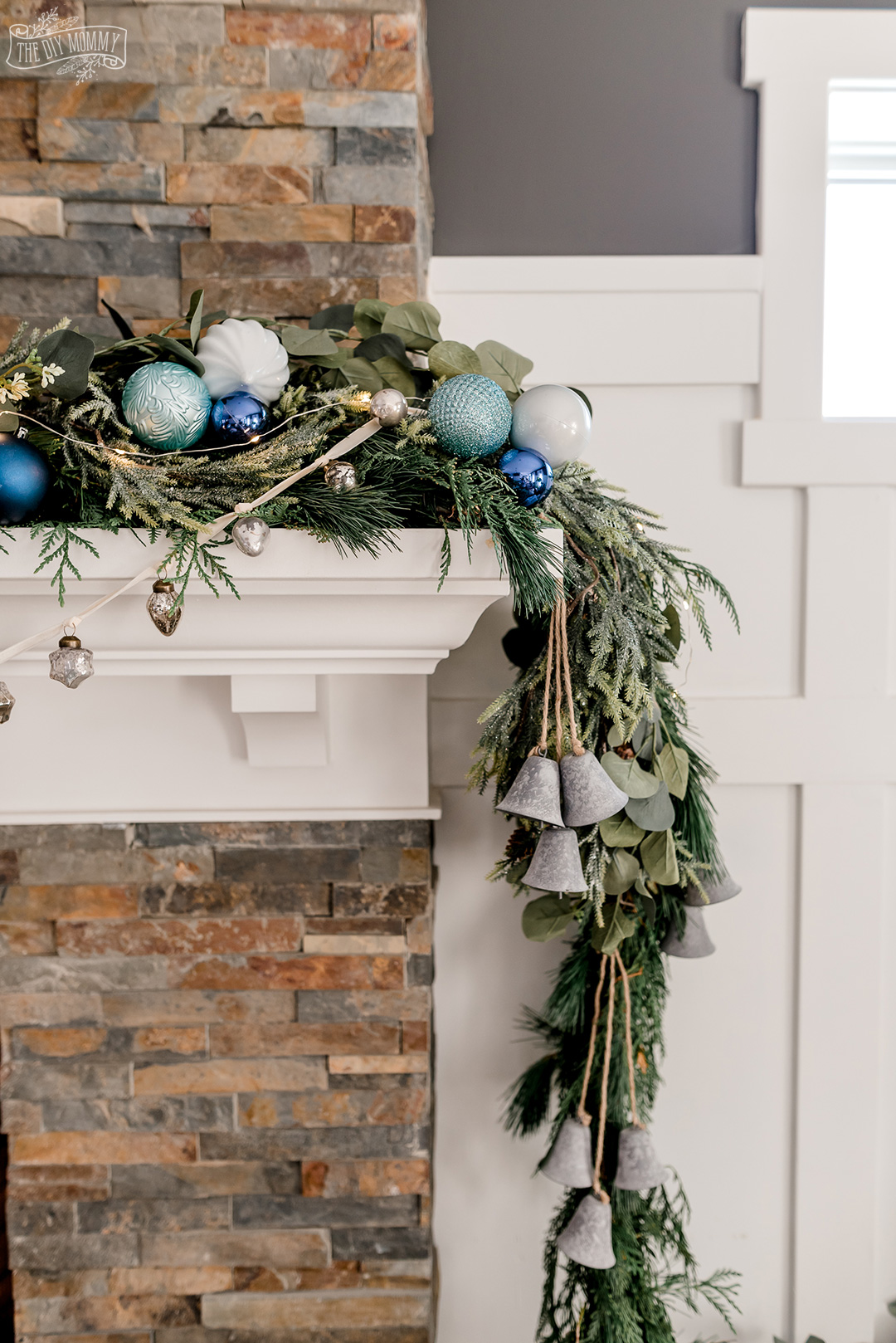 Christmas mantel with asymmetrical fresh greenery, blue colors, metallics, bottle brush trees and knit stockings.