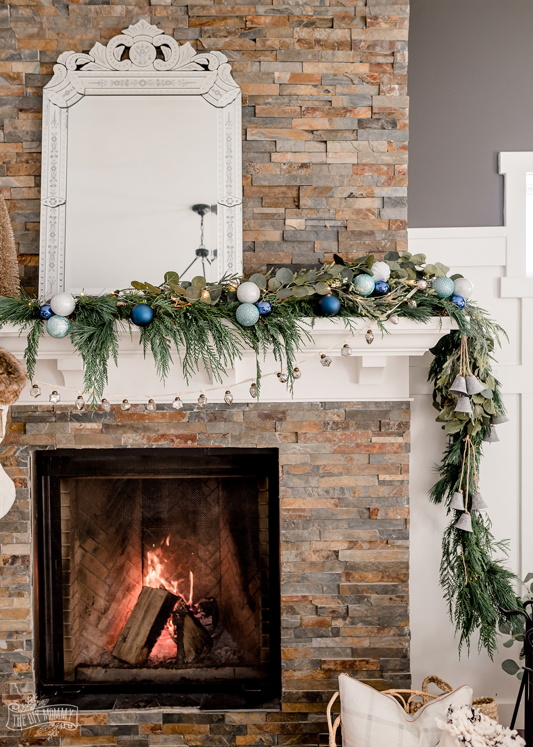 Christmas mantel with asymmetrical fresh greenery, blue colors, metallics, bottle brush trees and knit stockings.