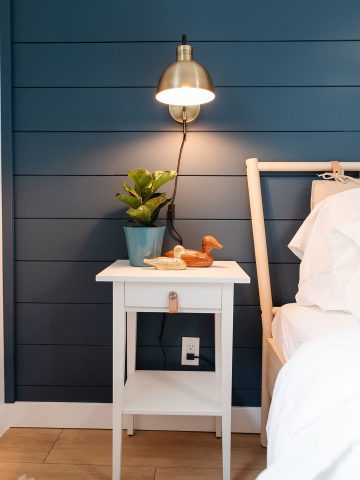 Modern coastal bedroom makeover with deep blue shiplap wall, vinyl plank flooring, IKEA furniture, and gold accents