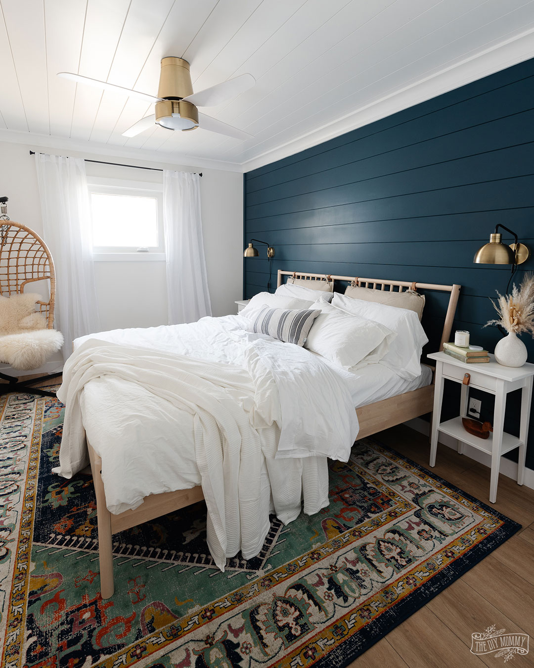 Modern coastal bedroom makeover with deep blue shiplap wall, vinyl plank flooring, IKEA furniture, and gold accents