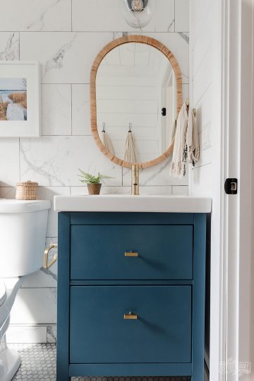 Modern coastal inspired bathroom renovation with marble tile, shiplap, gold and black accessories, clear shower door, blue and white colors & rattan accents