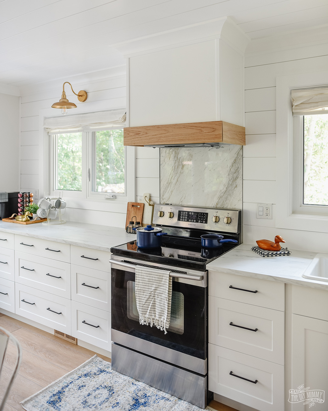 See how a dated honey oak kitchen was transformed into a coastal modern farmhouse kitchen with an eat-in layout, white shaker cabinets and white oak accents.