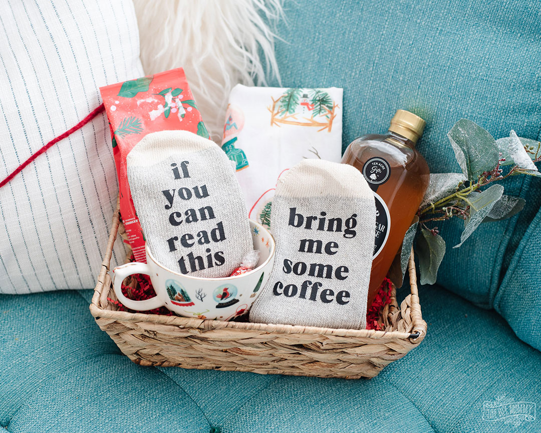 A wicker basket filled with a pair of personalized socks reading "if you can read this bring me some coffee" coffee and a bottle of sprits.