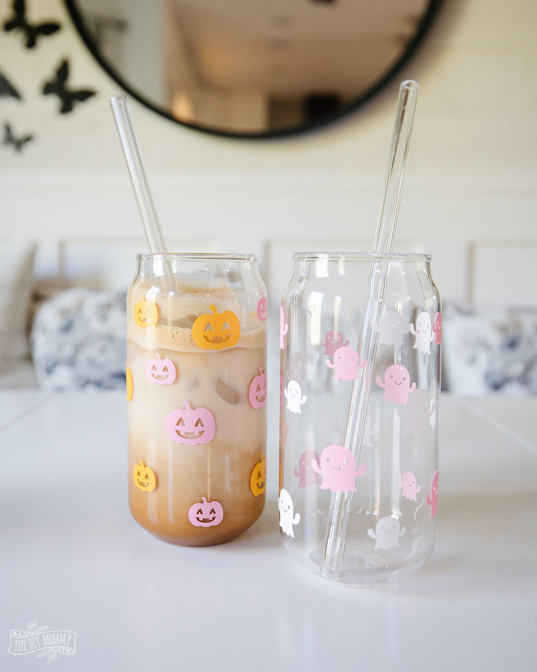 Two beer can glasses decorated with little cricut cut outs of pink and orange pumpkins and pink and white ghosts. Perfect for your indoor diy Halloween decorations
