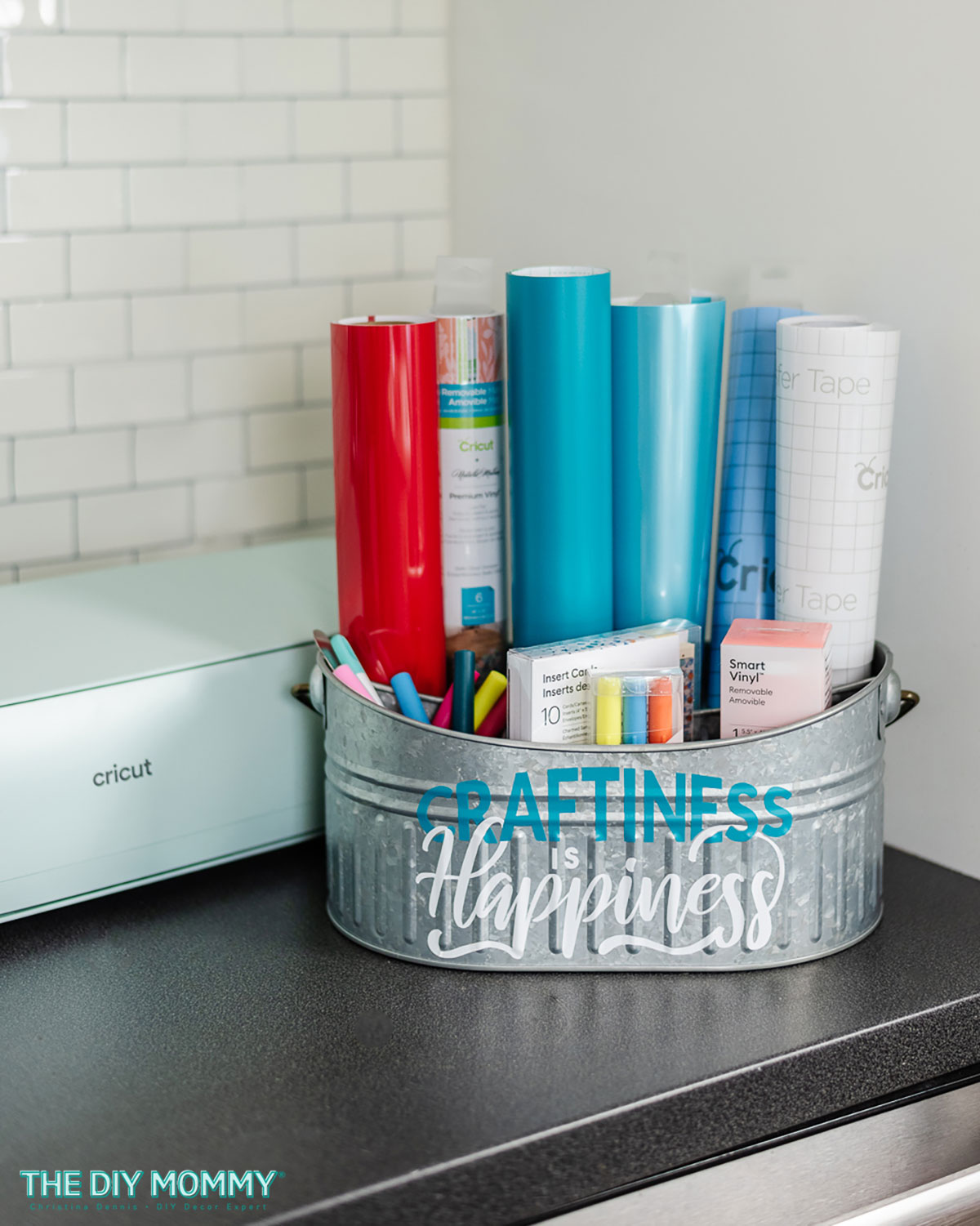 A cute little galvanized craft caddy with a custom decal reading "craftiness is happiness' full of art supplies.
