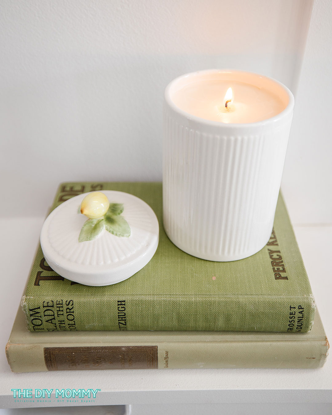 A  white ceramic thrift store cannister made into a candle, standing on a stack of books. A perfect idea for a teacher DIY Christmas gift