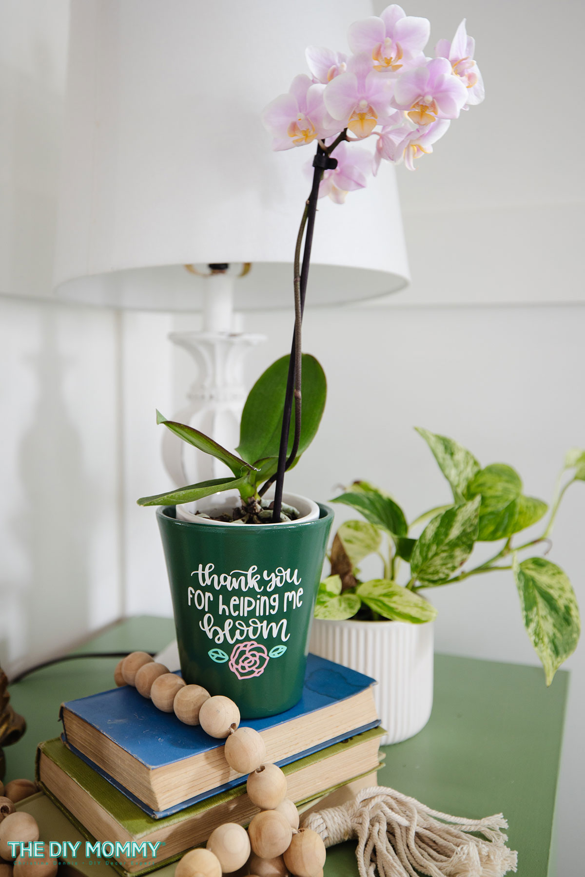 The personalized gardening gift of an orchid in a plant pot. The pot is decorated with a decal that reads "Thank you for helping me bloom."