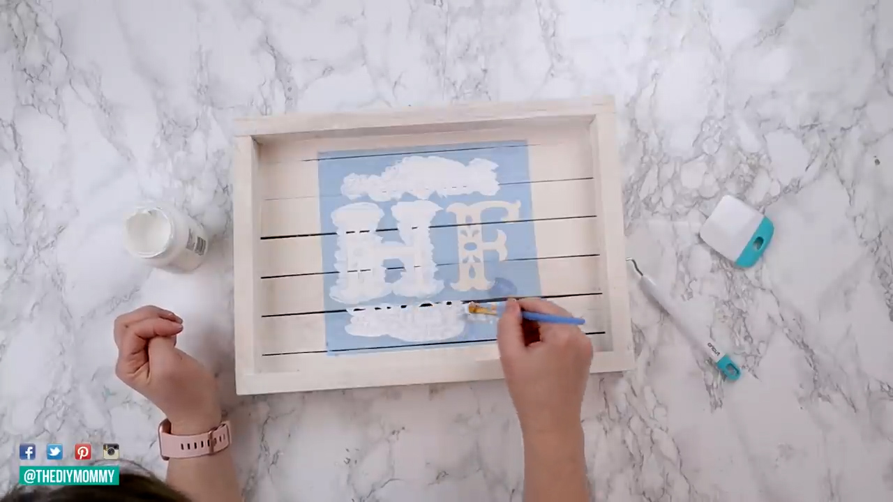 Christina paints a personalized blue stencil design, initials "HF" onto a wooden tray.