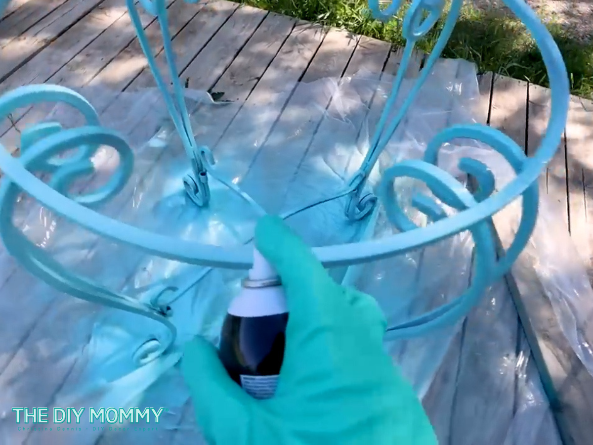 Christina is spraying a second coat of teal paint on the base of the thrifted iron table. 